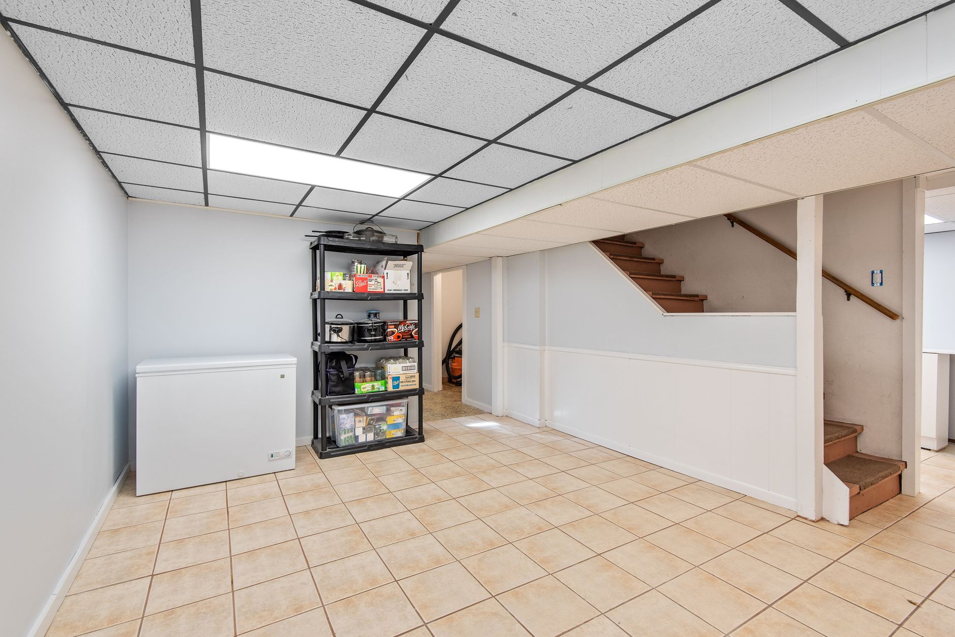 Basement lower level with tile flooring, storage shelving, and stairs