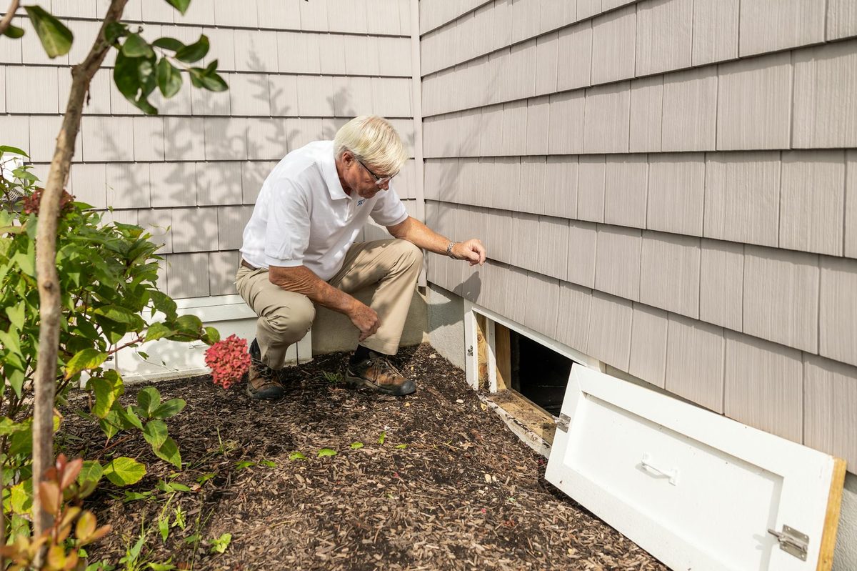 Inspector opening an exterior crawl space access door at a home