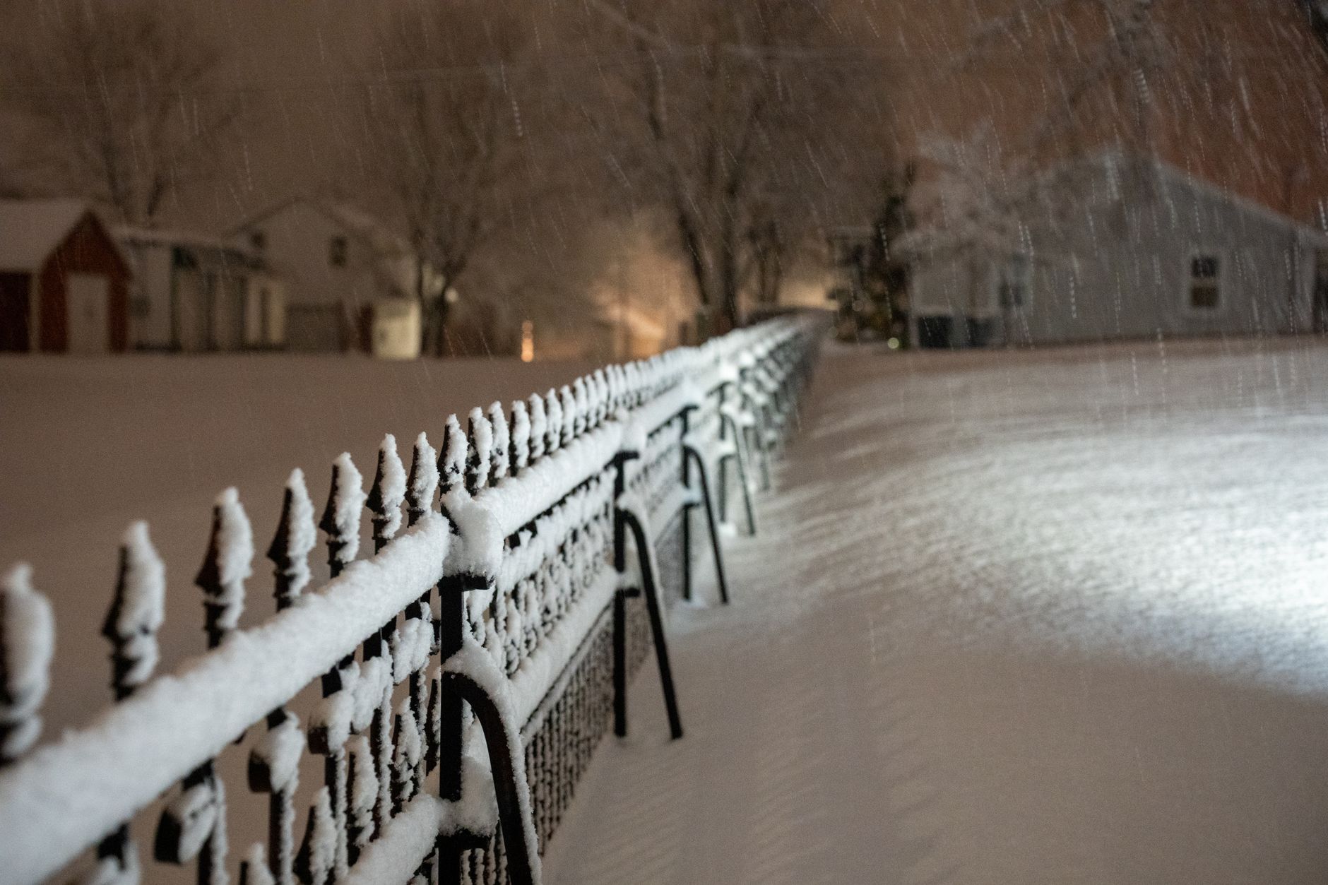Snow accumulating on a fence in front of houses during a night snowfall
